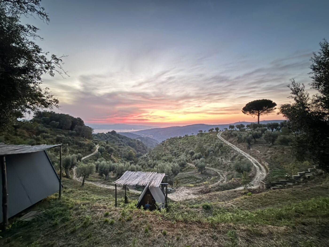 Tenda A-frame di Gaya sotto cielo rosato, sentieri serpeggianti sulle colline