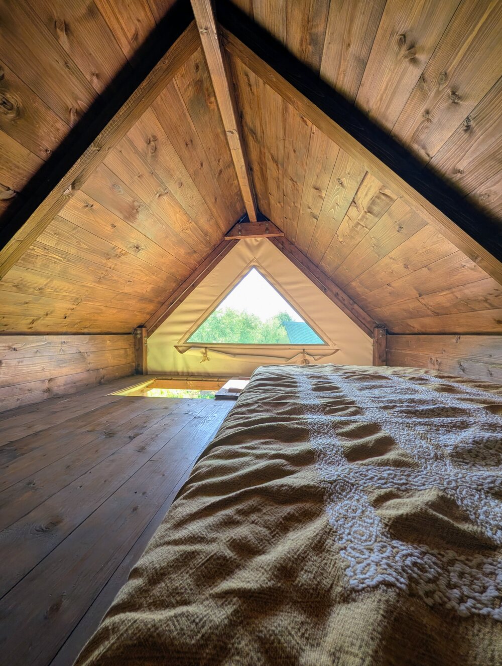 Interno di un Nido a palafitta di Gaya: letto e finestra triangolare sul bosco