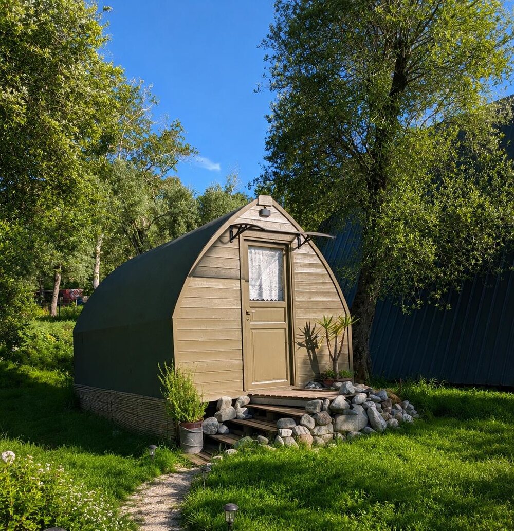 Il Seme di Gaya: cabina di legno col tetto a sesto acuto, scalini di pietre, alberi attorno
